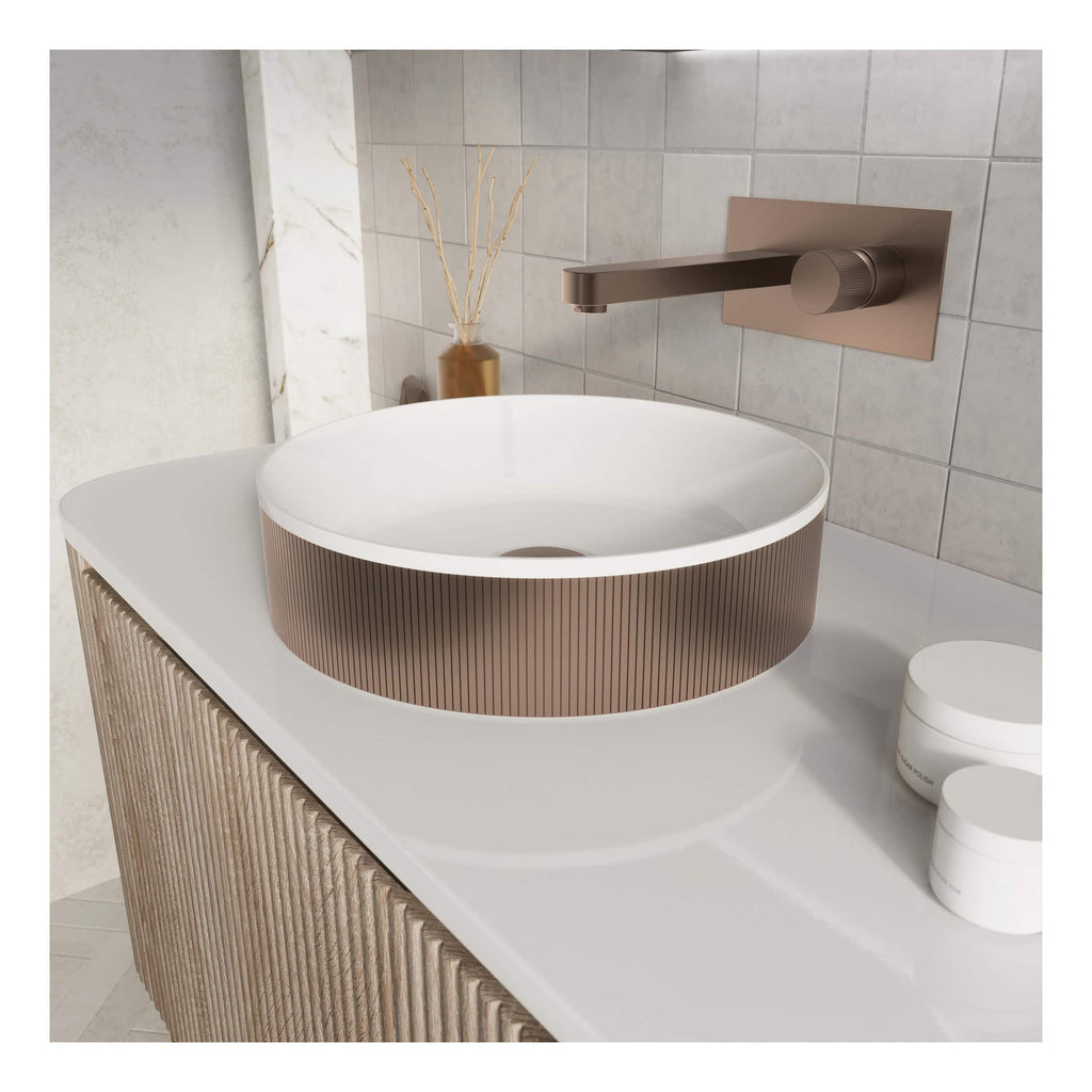 Sleek modern bathroom sink with a round vessel basin and copper-toned textured exterior, mounted on a white countertop with a matte bronze wall-mounted faucet, complemented by minimalist decor.