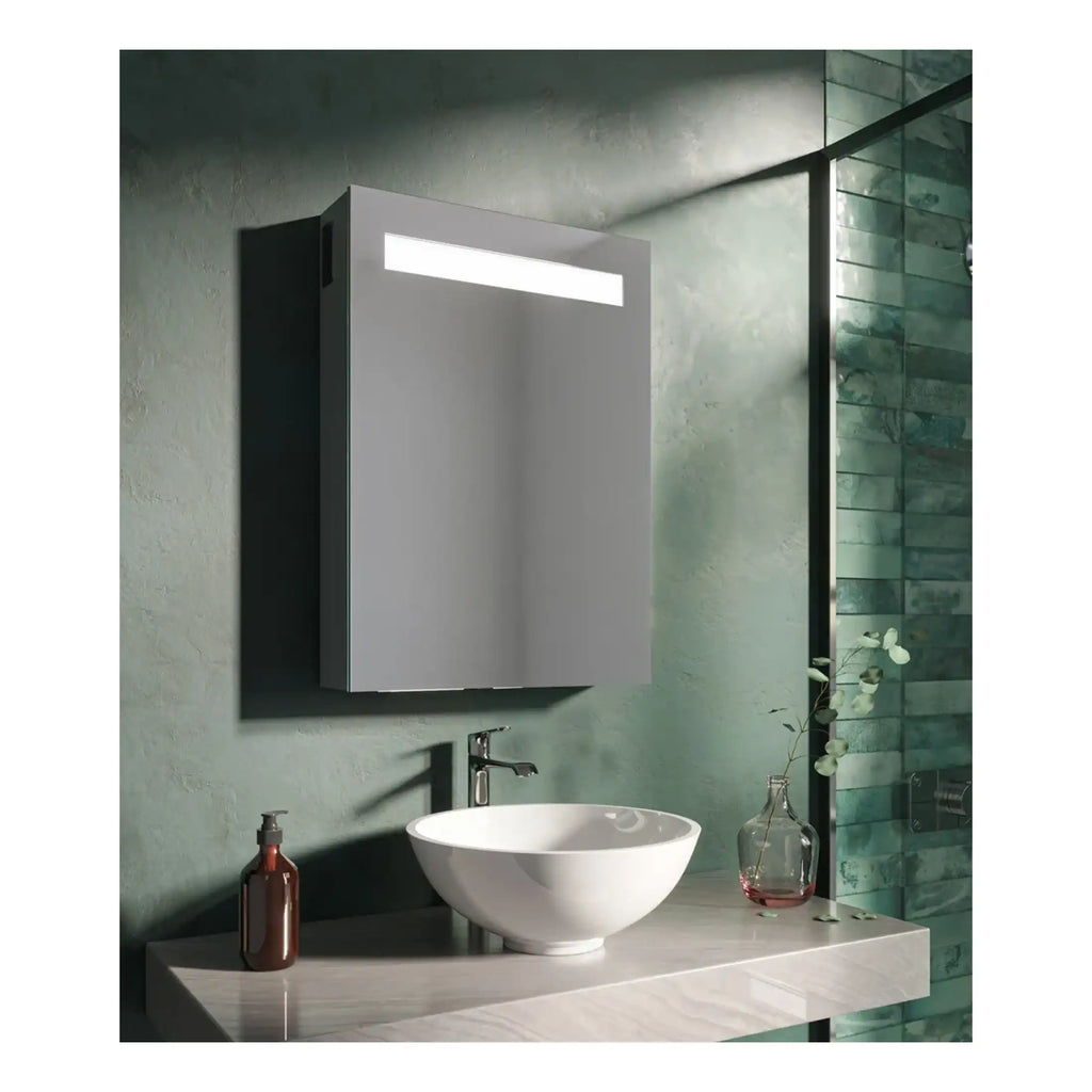 Sleek grey bathroom mirror cabinet with integrated lighting above a modern white vessel sink on a marble countertop, set against a textured green wall with a glass shower enclosure.