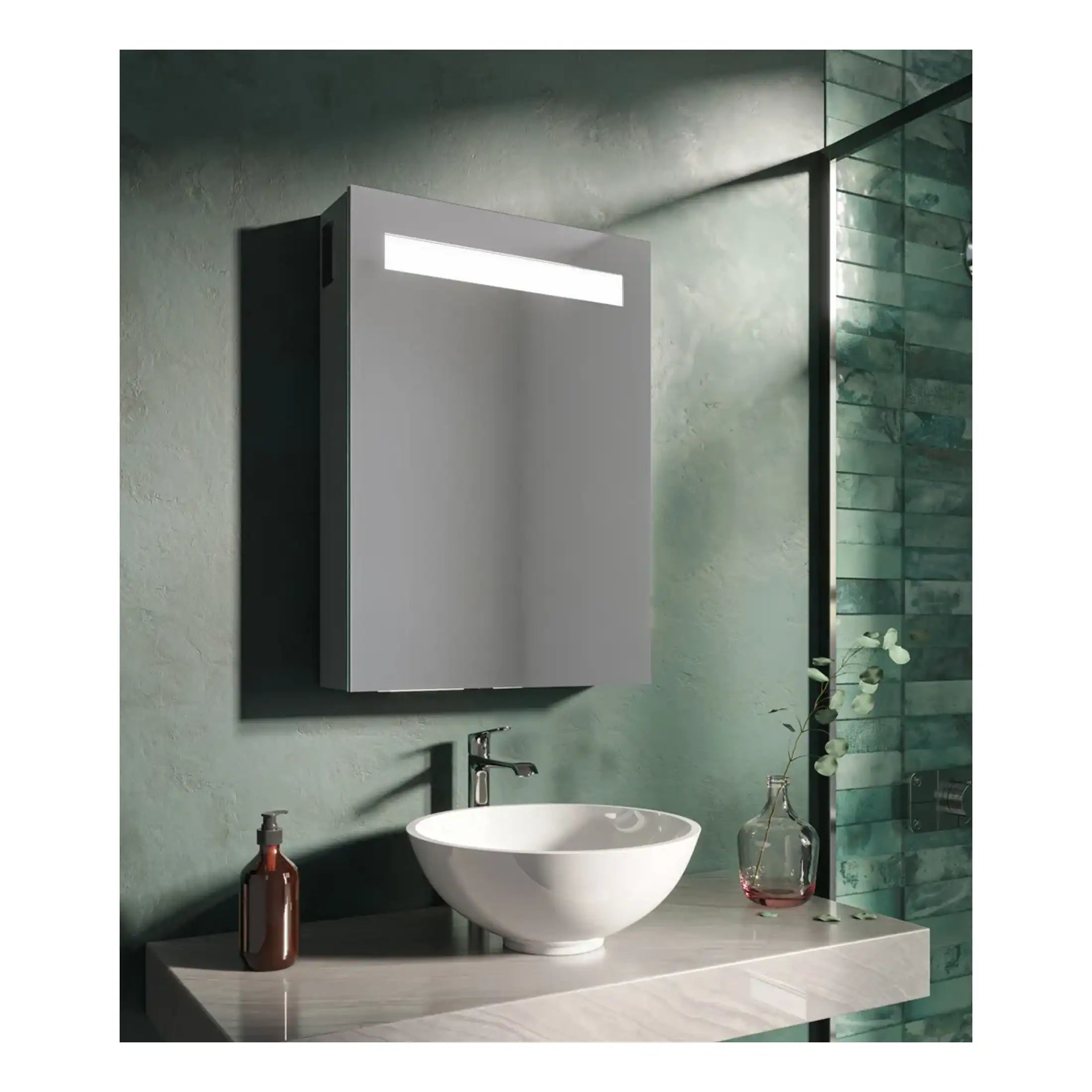 Sleek grey bathroom mirror cabinet with integrated lighting above a modern white vessel sink on a marble countertop, set against a textured green wall with a glass shower enclosure.