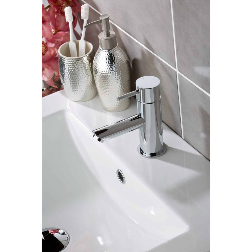 Sleek modern chrome bathroom tap with silver soap dispenser and toothbrush holder on a white sink, featuring a grey tiled wall background, showcasing contemporary bathroom design and fixtures.