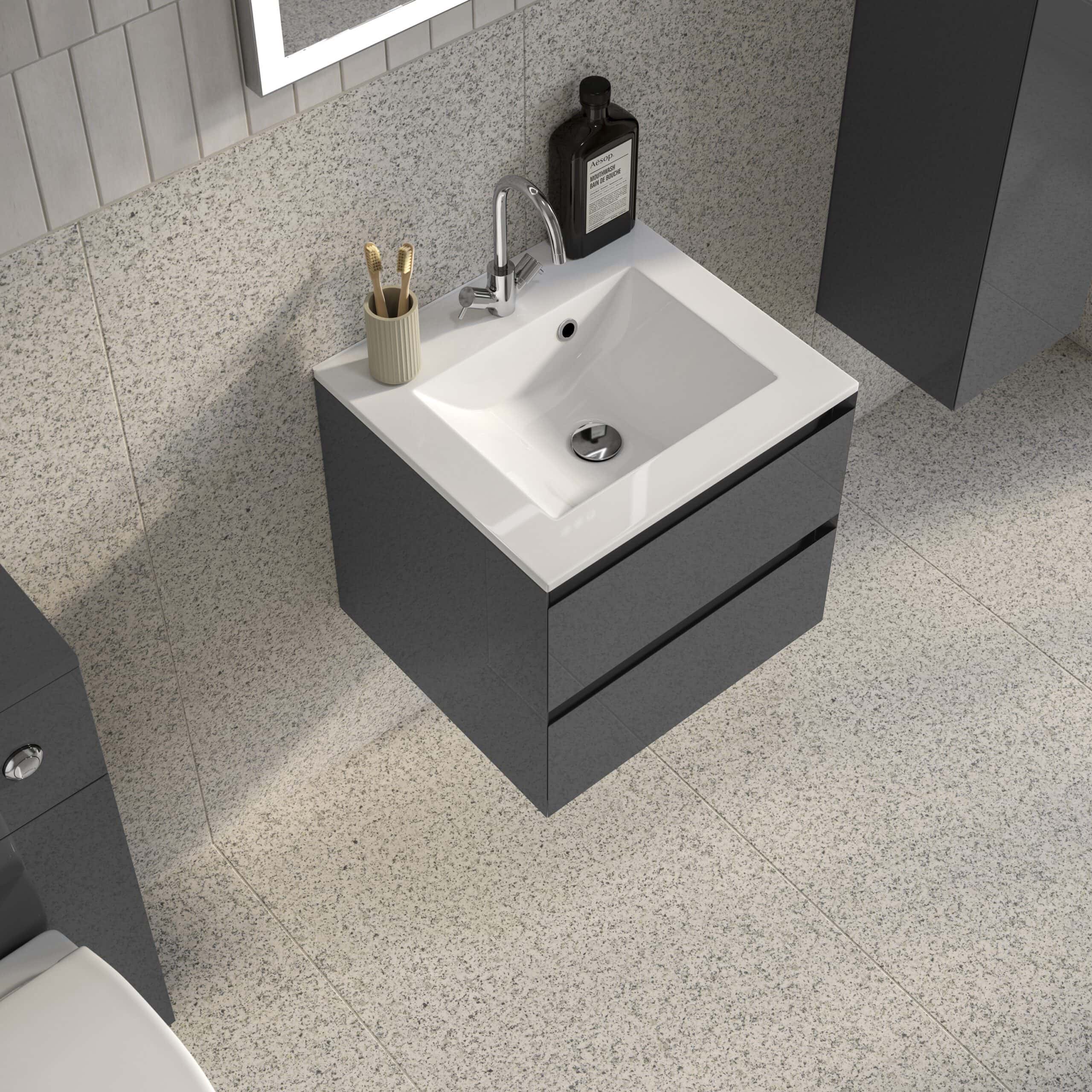 Sleek modern bathroom vanity with a white ceramic sink, dark grey cabinet, chrome tap, and bathroom essentials on top, set against tiled walls and flooring.