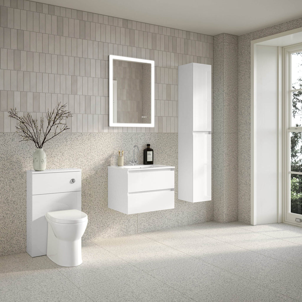 Modern white bathroom with a sleek vanity unit, illuminated mirror, wall-mounted toilet, and tall storage cabinet, featuring neutral tiled walls and natural light from a large window.