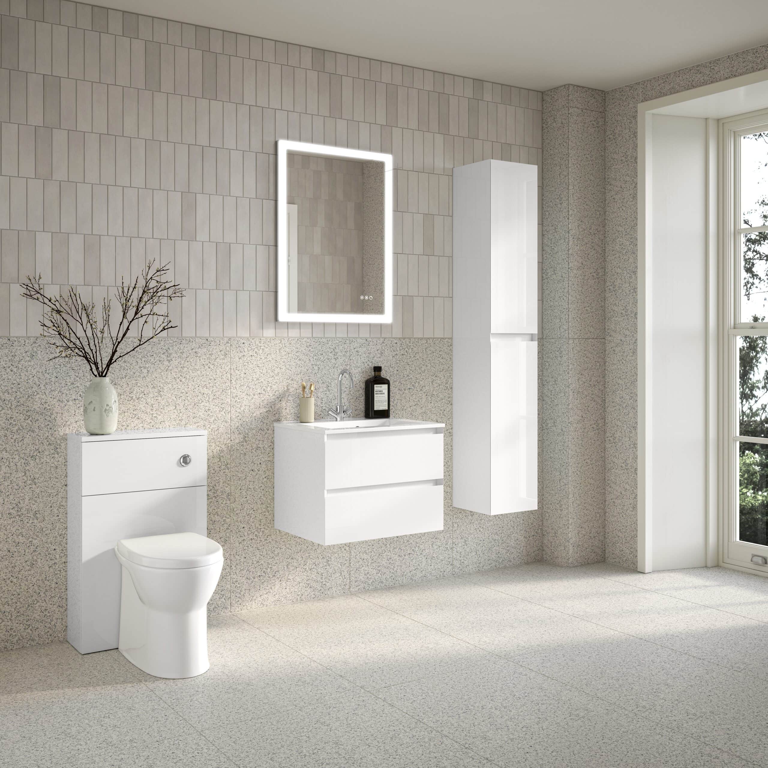Modern white bathroom with a sleek vanity unit, illuminated mirror, wall-mounted toilet, and tall storage cabinet, featuring neutral tiled walls and natural light from a large window.