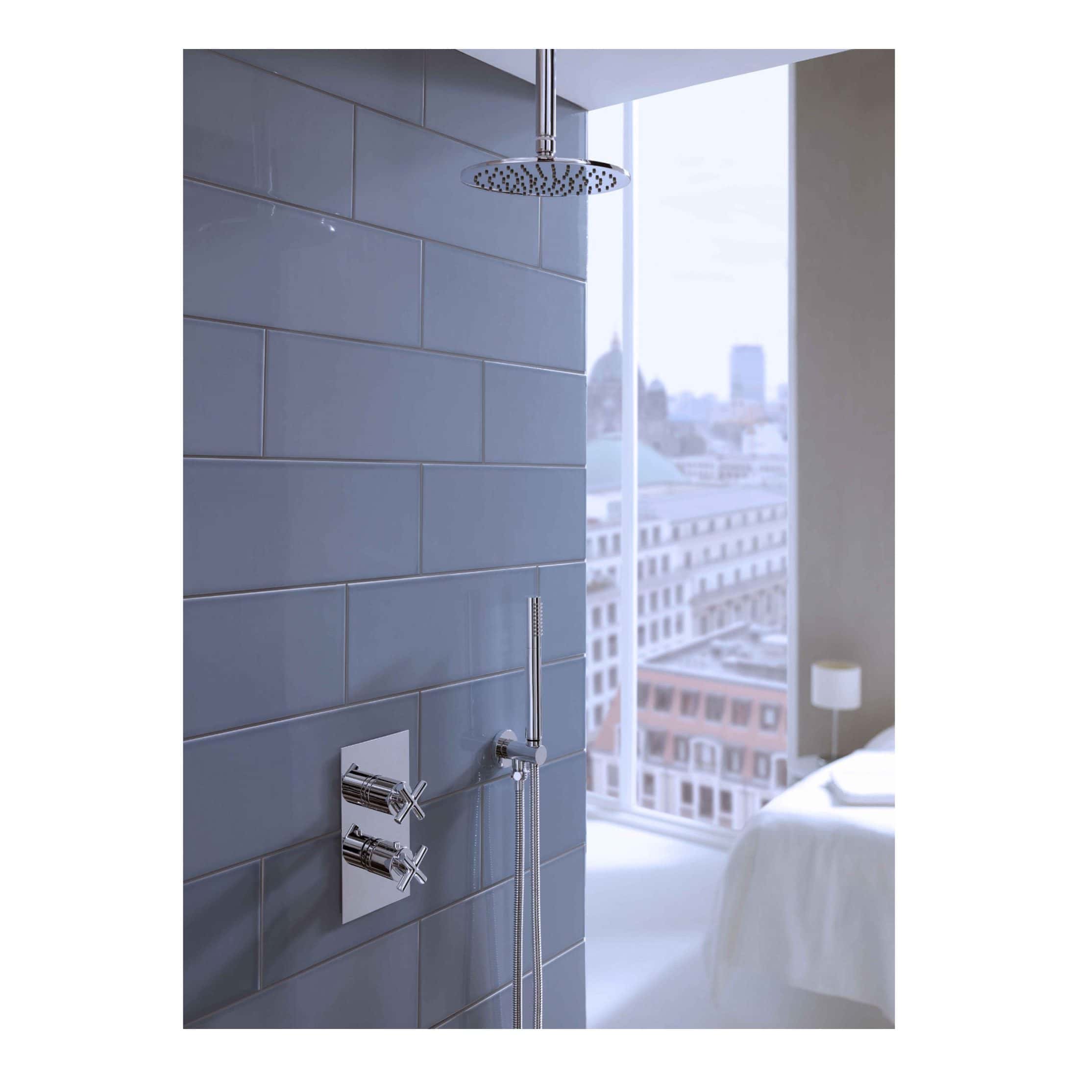 Sleek modern rainfall shower head and chrome controls in a contemporary bathroom with blue subway tiles and city view window.