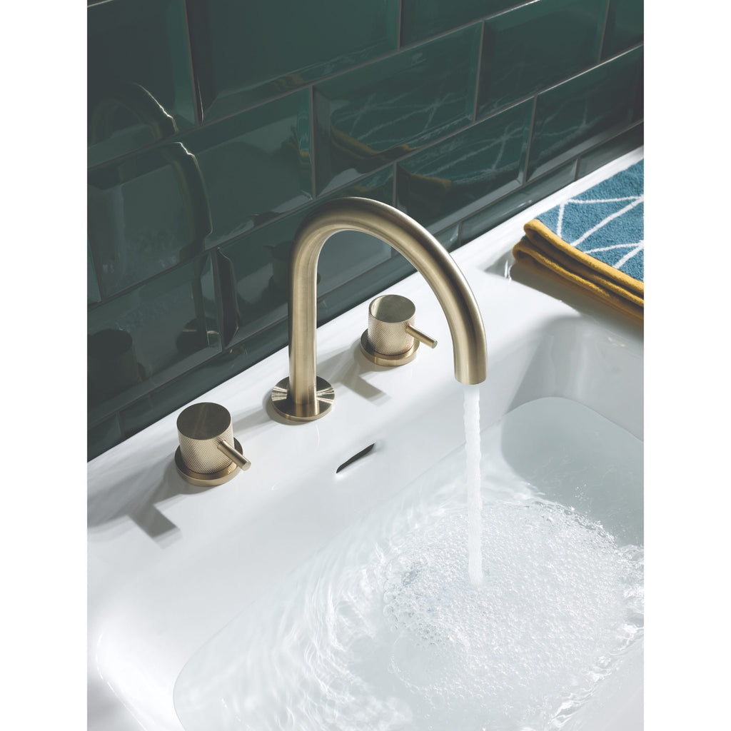 Sleek brushed brass bathroom tap with water flowing into a white bathtub, modern black tiled wall, and a navy and yellow towel, showcasing stylish bathroom fixtures and accessories for a contemporary look.