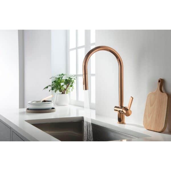 Sleek rose gold kitchen tap over white countertop with sink, natural light from window, green plant, and wooden cutting board, modern bathroom or kitchen design.