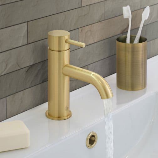 Shiny gold bathroom tap with flowing water on a white sink.