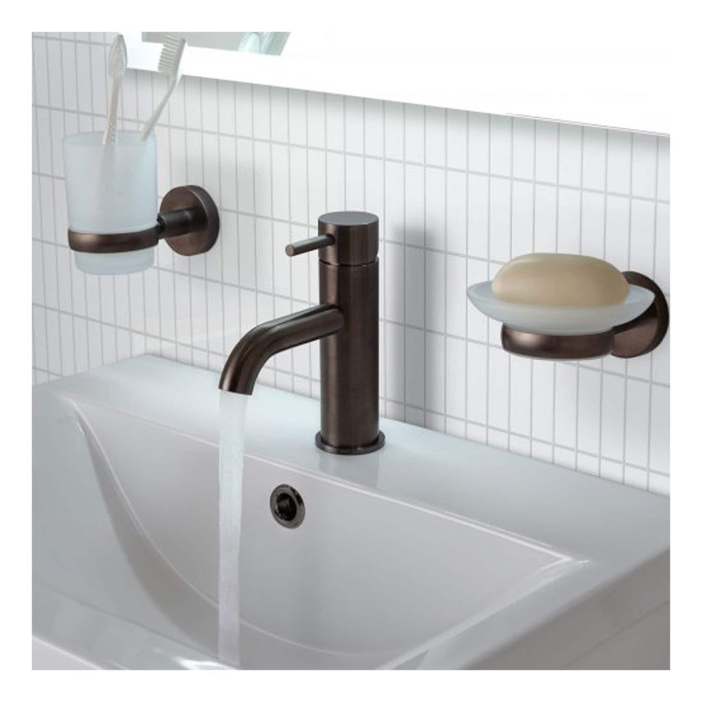 Sleek modern bathroom sink with bronze finish tap, wall-mounted soap dish, and toothbrush holder on a white tiled wall, creating a stylish and functional bathroom setup.