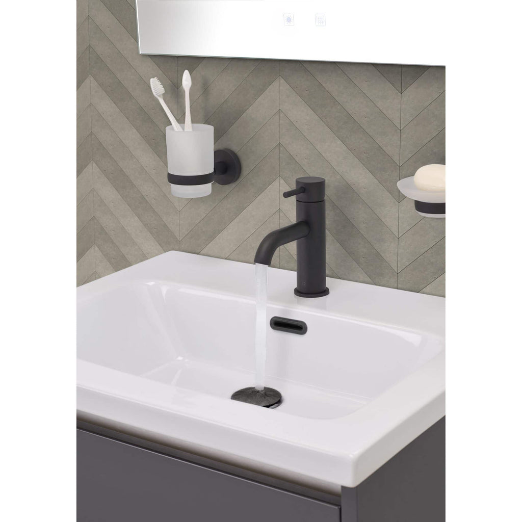 Modern bathroom sink with black matte tap and accessories, featuring storage for toiletries and toothbrushes, against a stylish chevron tile wall. Perfect for contemporary bathroom decor and vanity setups.