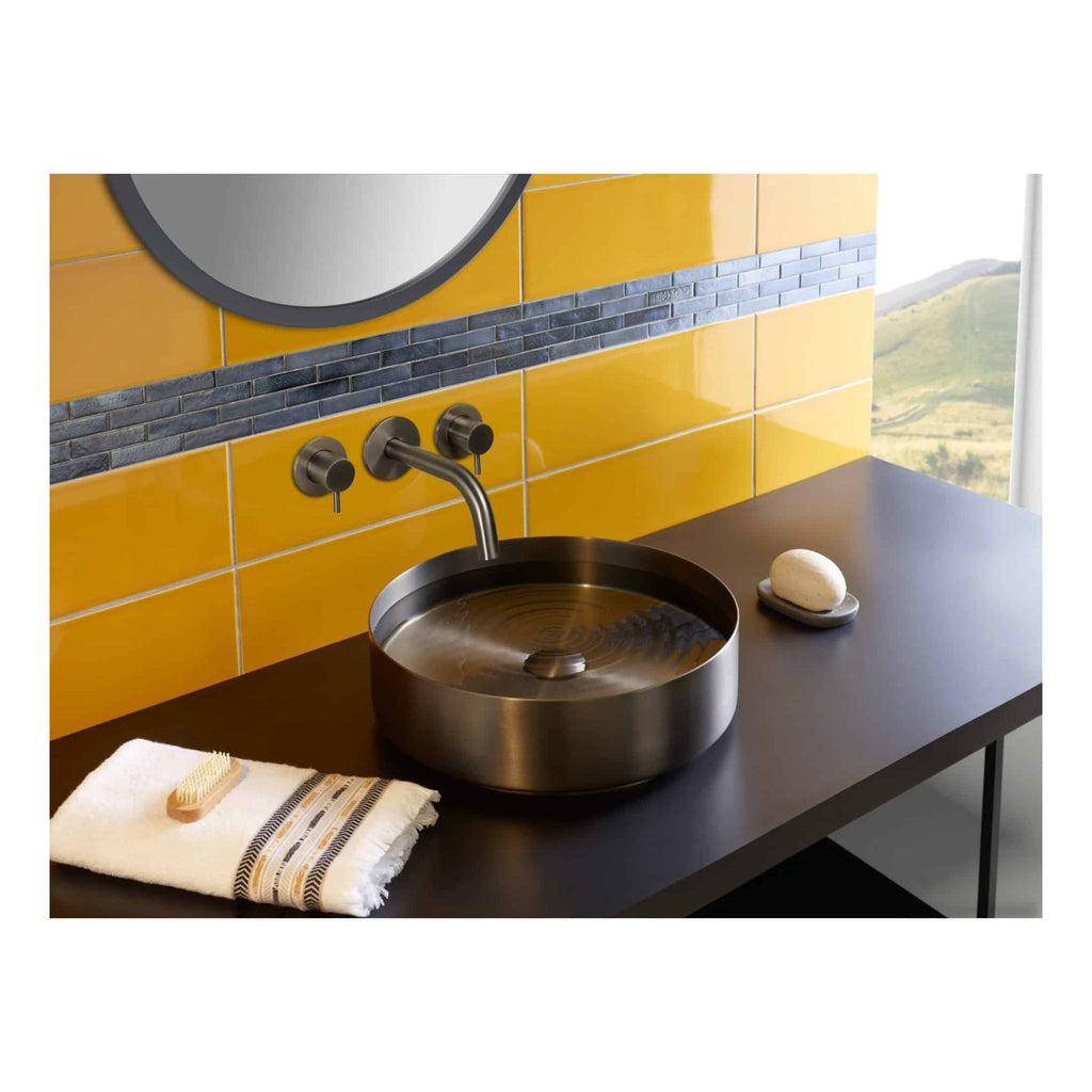 Polished stainless steel bathroom sink with wall-mounted tap in a modern bathroom setting featuring yellow tiled wall with blue accent tiles.