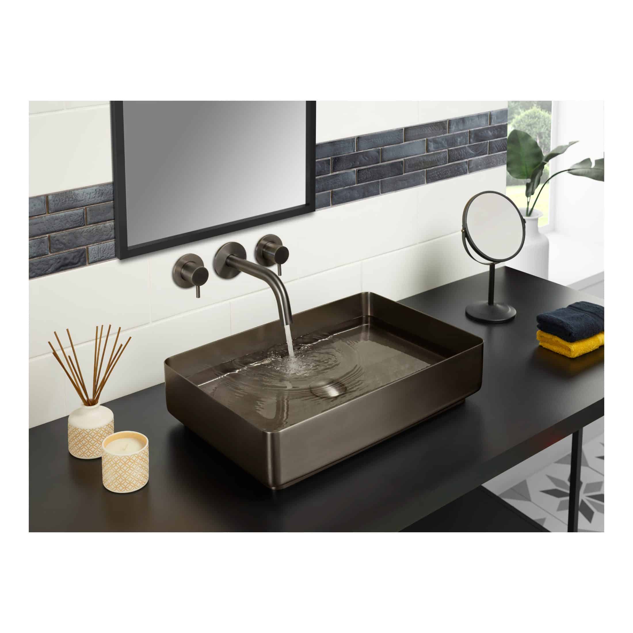 Sleek bronze bathroom basin with modern wall-mounted tap, surrounded by stylish decor including candles, reed diffuser, and a small mirror, set against a contemporary tiled wall. Perfect for elegant bathroom design.