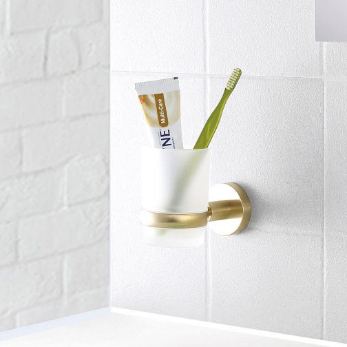 Toothpaste and toothbrush holder mounted on a white tiled bathroom wall, showcasing modern bathroom accessories.