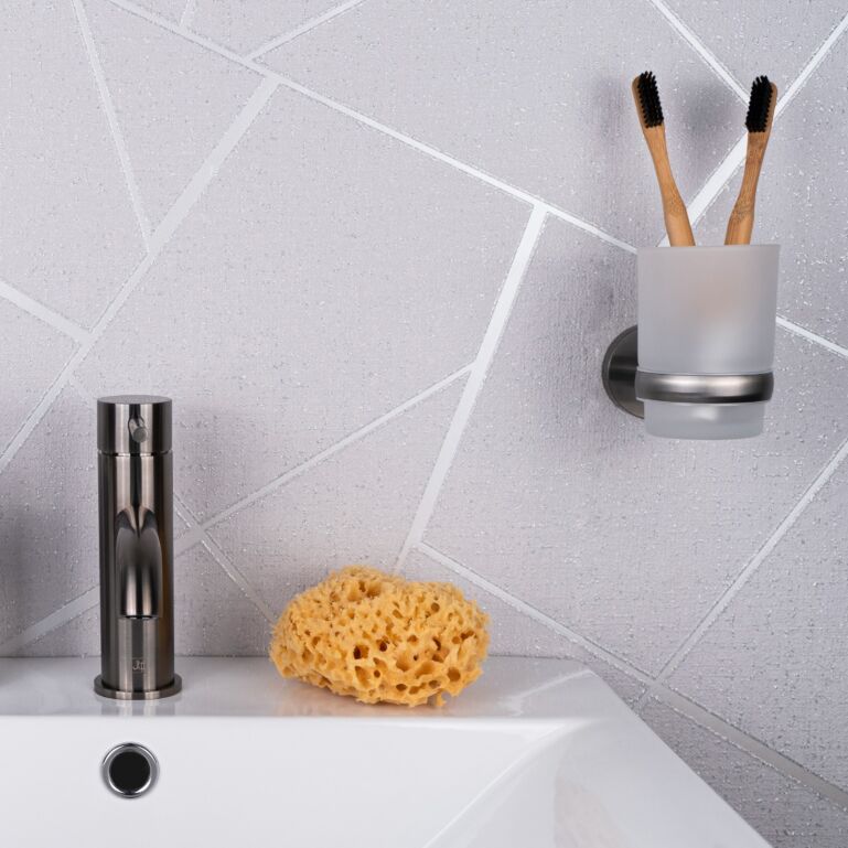 Stainless steel bathroom sink tap with a natural sponge and toothbrush holder mounted on a tiled wall, showcasing modern bathroom fixtures.