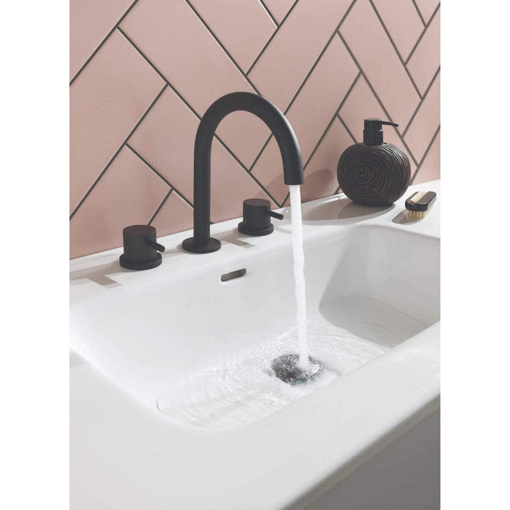 Sleek black bathroom tap and fixtures with running water in modern white sink against pink tiled wall, showcasing elegant bathroom design.