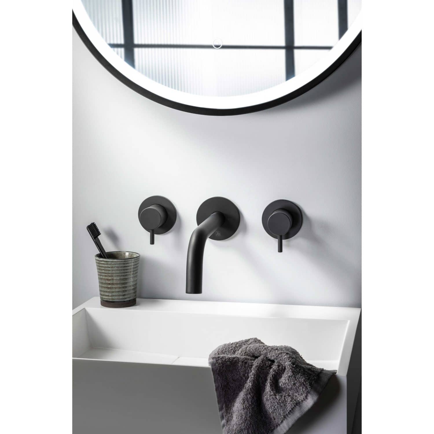Minimalist black bathroom taps and fixtures above white ceramic sink with a towel and toothbrush holder, modern bathroom decor, elegant black wall-mounted tap set for contemporary bathroom design.