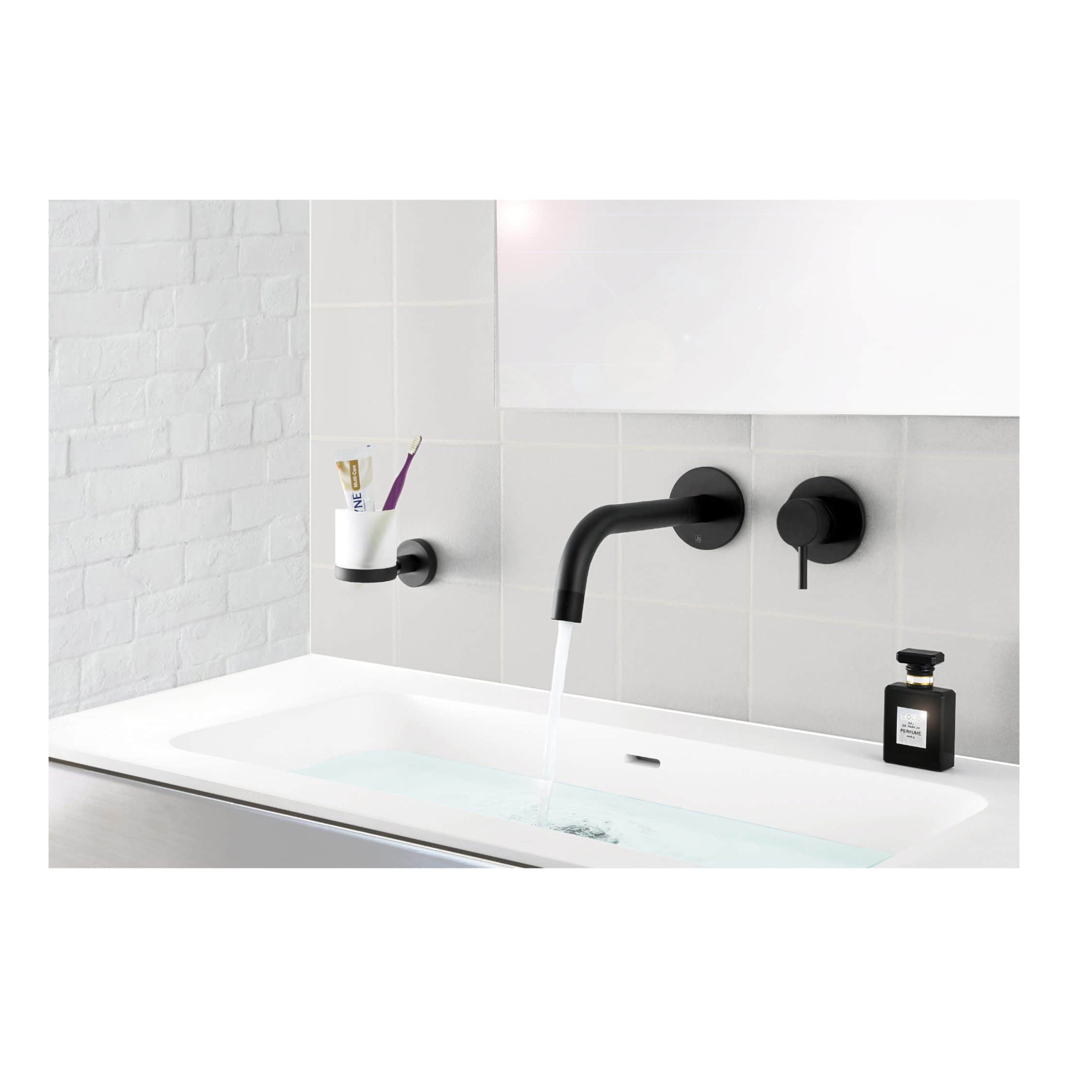 Sleek black matte bathroom faucet with integrated controls, mounted above a modern white bathtub with water running, complemented by a black soap dispenser and toothbrush holder on a tiled wall.