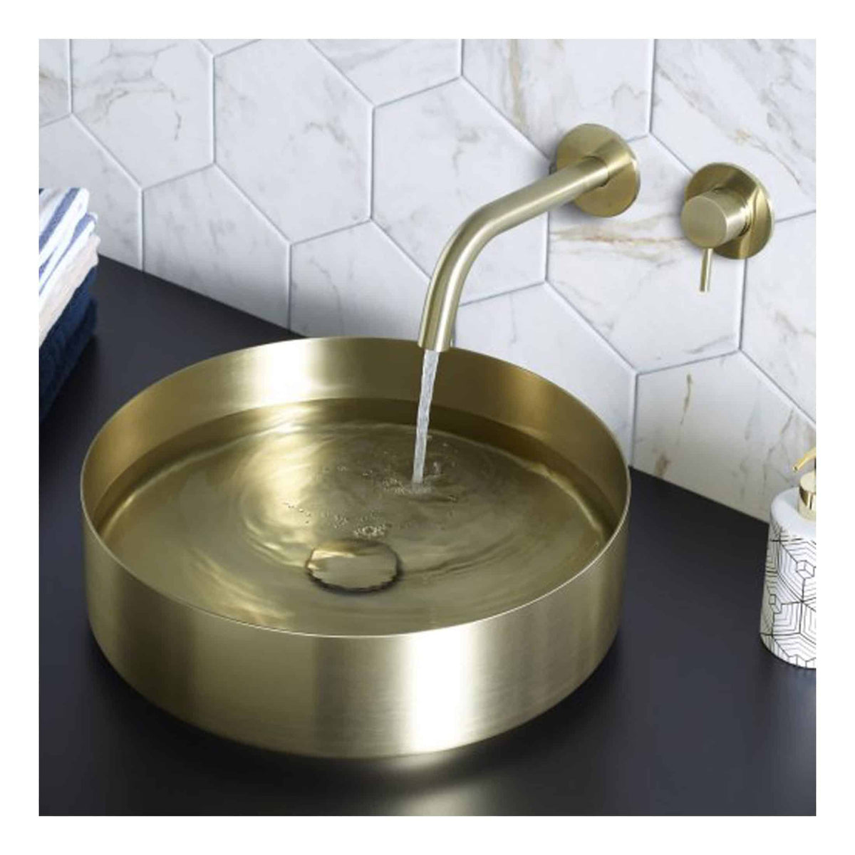 Shiny gold bathroom sink with water running, modern bronze tap, and hexagonal marble wall tiles. Elegant bathroom vanity setup with stylish fixtures. Perfect for contemporary bathroom renovation ideas.