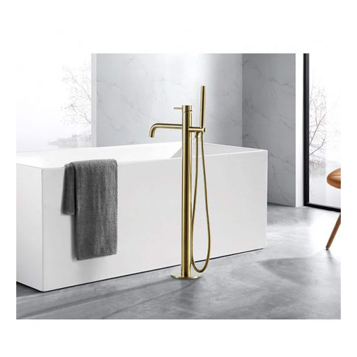 Polished gold freestanding bathtub filler with a hand shower, modern bathroom decor with white bathtub, grey towel, marble wall, and minimalist design in a contemporary bathroom setting.