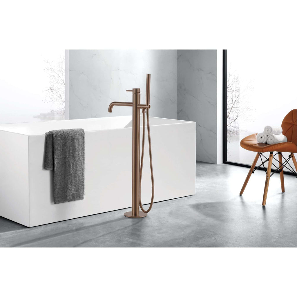 Bronze freestanding bathroom faucet with a matching handheld shower, next to a modern white bathtub in a minimalist bathroom with grey flooring and marble wall accents.