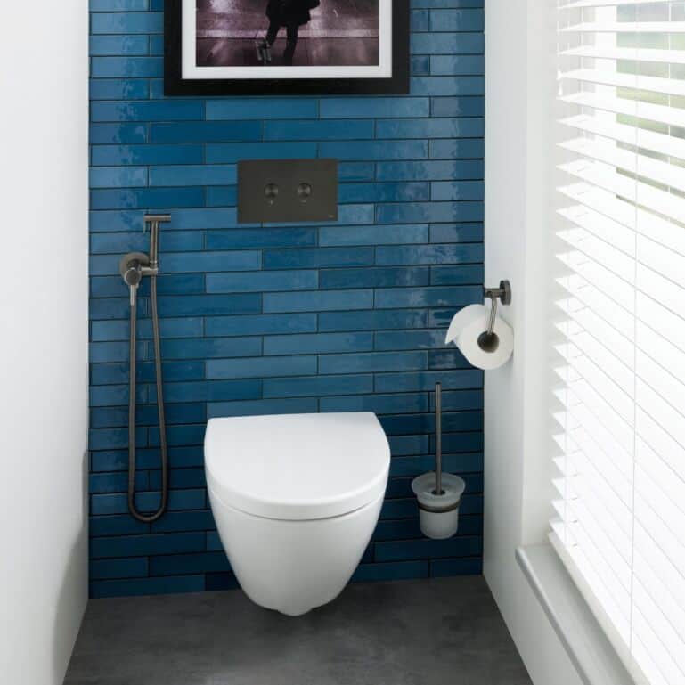 Blue tiled bathroom wall with modern white toilet, bidet spray, and toilet brush holder. Bright, minimalistic design perfect for contemporary Bubly Bathrooms.