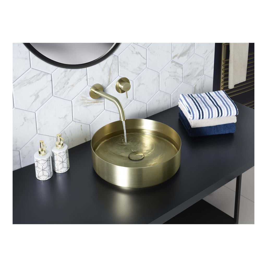 Brass bathroom sink with countertop, white hex tile wall, modern washbasin setup, bathroom decor with toiletries and textiles, stylish and contemporary bathroom design.
