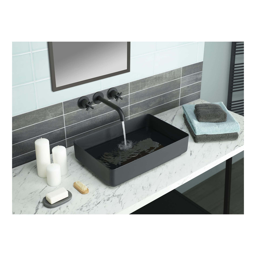 Contemporary black bathroom vessel sink with wall-mounted matte black faucet, set on a marble vanity with decorative candles, towels, and bath accessories, in a modern bathroom interior.