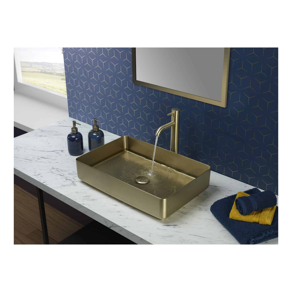 Luxury brass bathroom sink with modern brass tap on a marble countertop, blue and yellow towels, dark blue soap dispensers, and geometric wallpaper at Bubly Bathrooms UK.