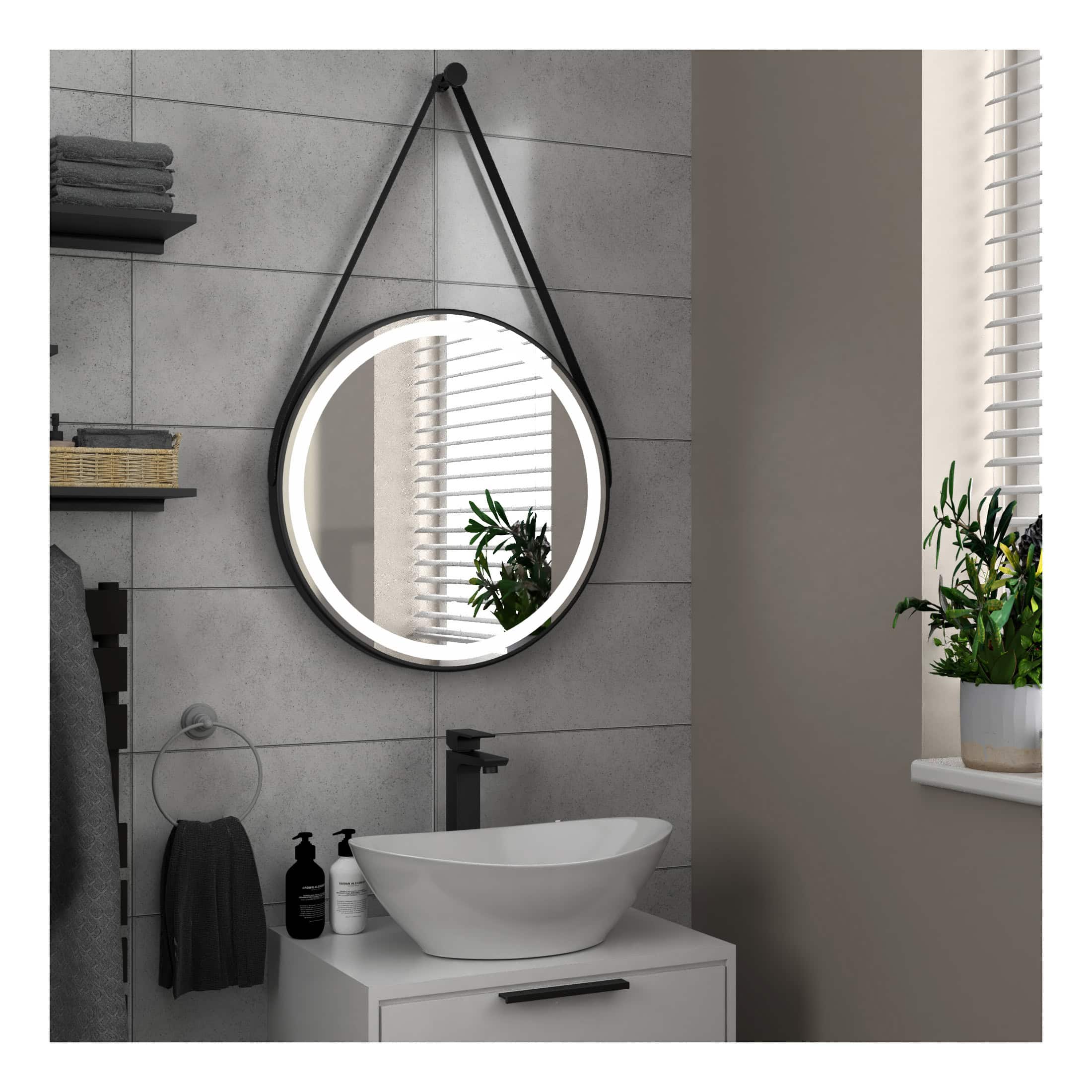 Round LED bathroom mirror with black leather strap hanging system, modern minimalist design, ideal for contemporary bathrooms, reflects natural light from nearby window.