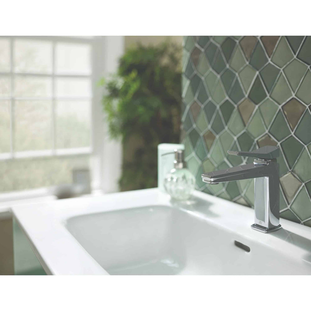Shiny modern kitchen tap above a white sink with a green geometric tile backsplash and a window with natural light.