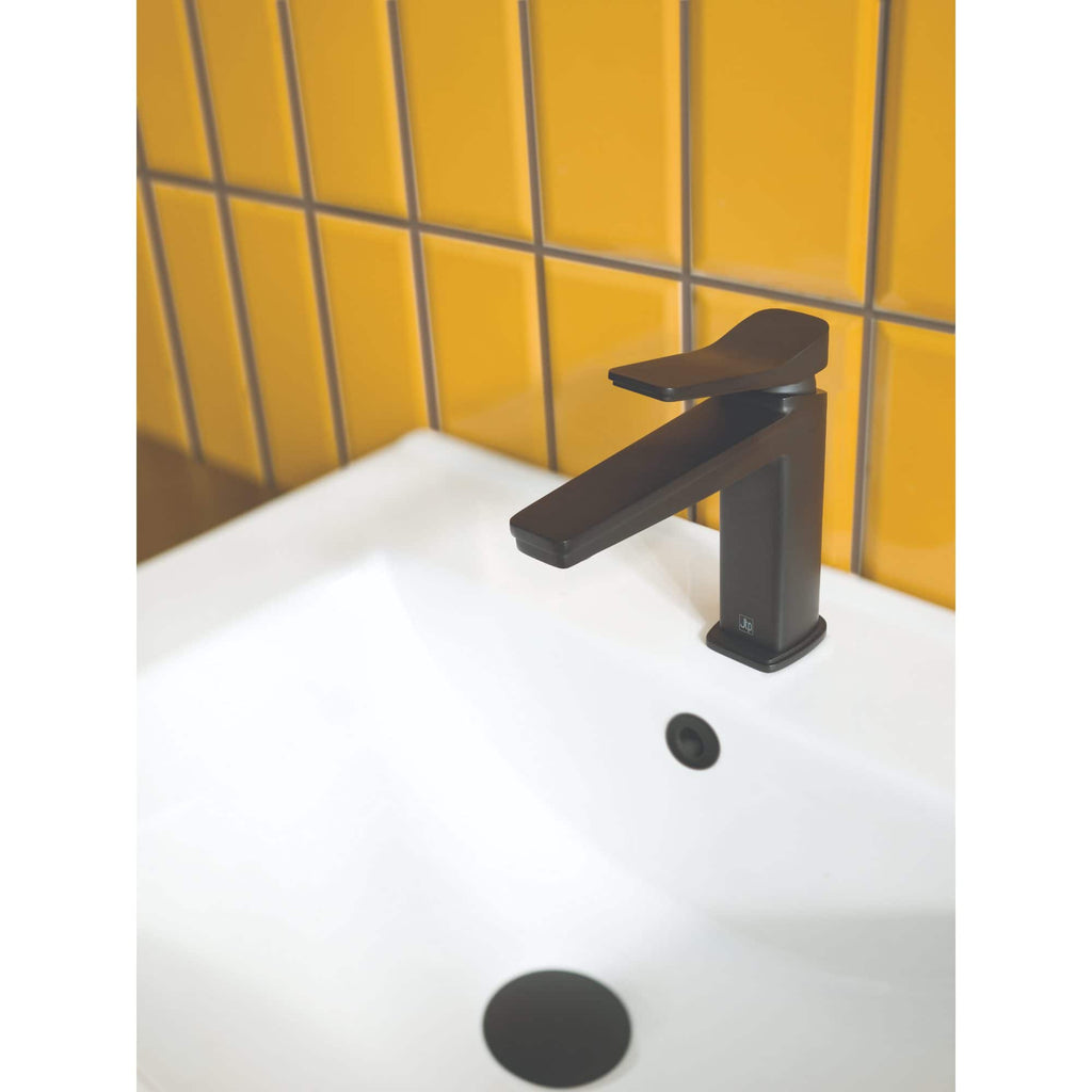 Modern black bathroom mixer tap installed on a white basin with yellow tiled wall background.