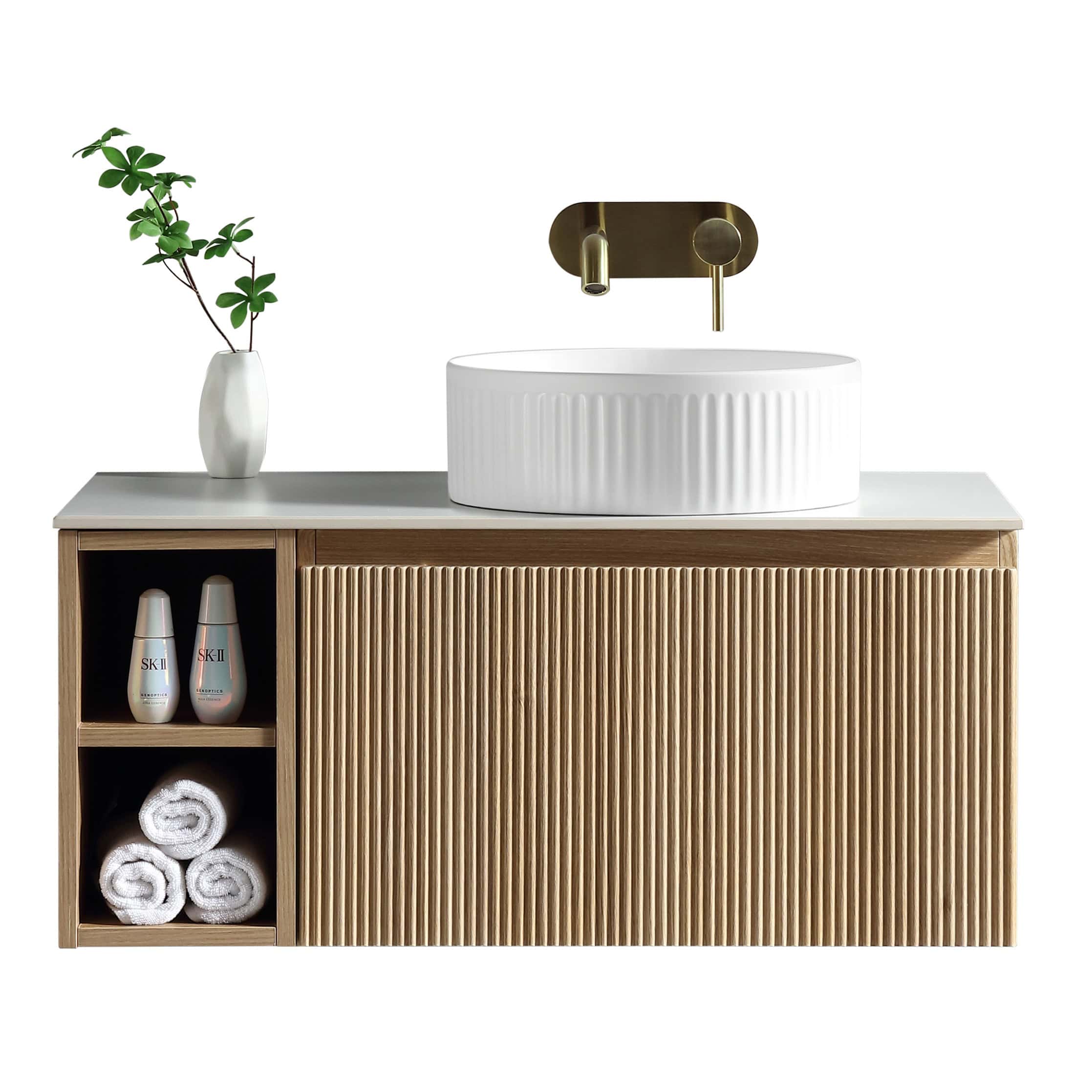 Contemporary bathroom vanity with ribbed oval white sink, gold wall-mounted tap, minimalist white vase with greenery, and storage with towels and skincare products, designed by Bubly Bathrooms.