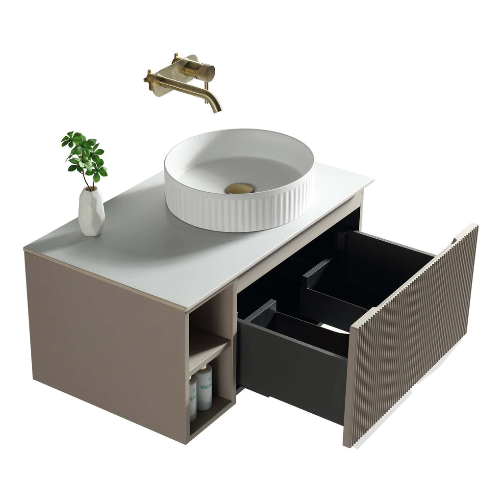 Modern bathroom vanity with round ceramic sink, brass wall-mounted faucet, minimalist storage cabinet with open shelves and black drawers, complemented by a white vase with green foliage.