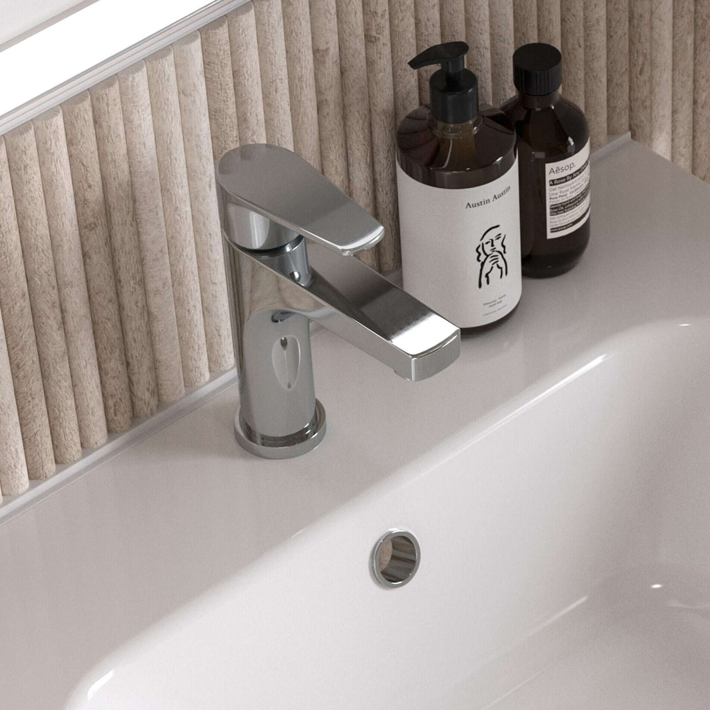 Shiny chrome bathroom sink tap with beige textured wall behind, accompanied by stylish white and brown bathroom toiletries bottles on a sleek white bathroom vanity.