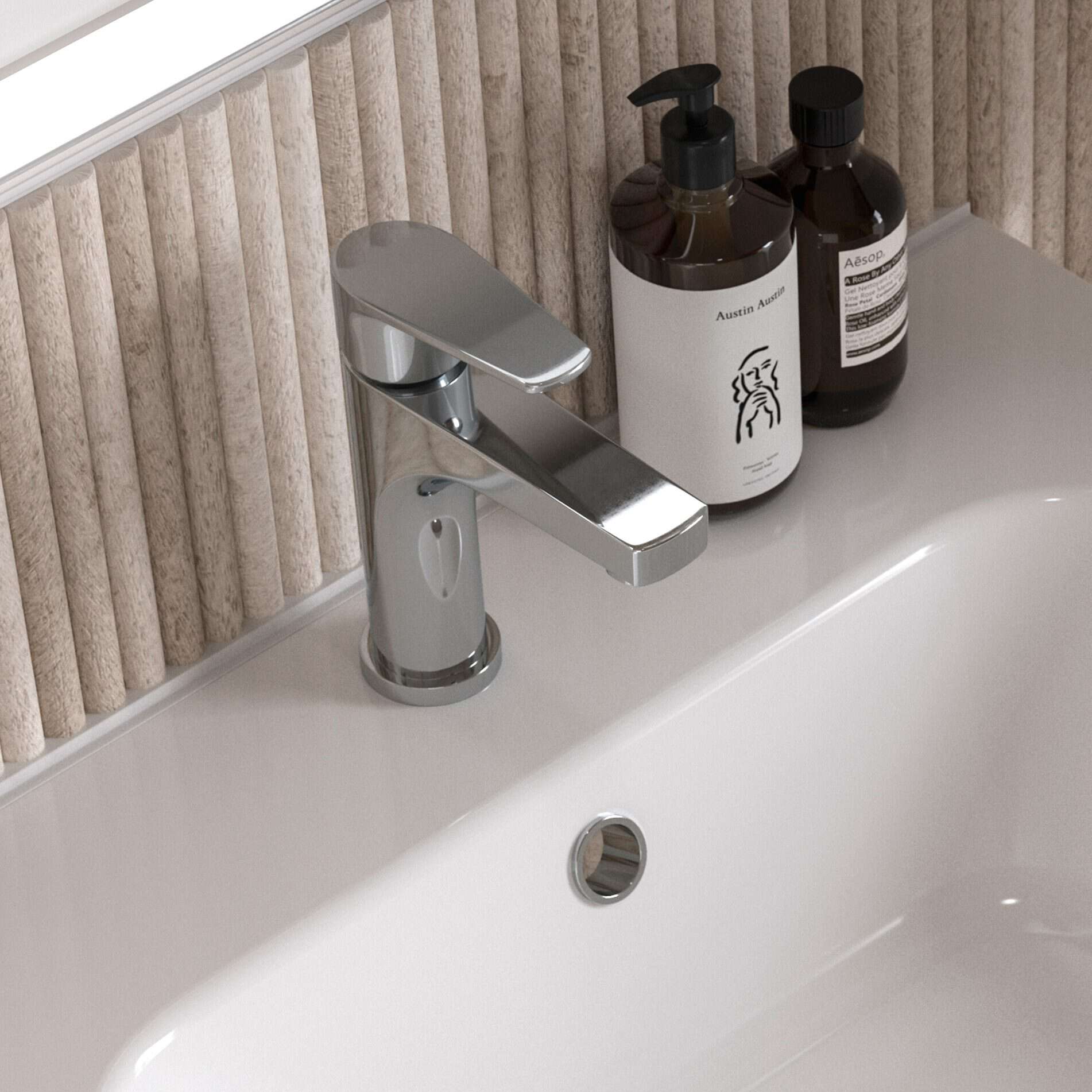 Shiny chrome bathroom sink tap with beige textured wall behind, accompanied by stylish white and brown bathroom toiletries bottles on a sleek white bathroom vanity.