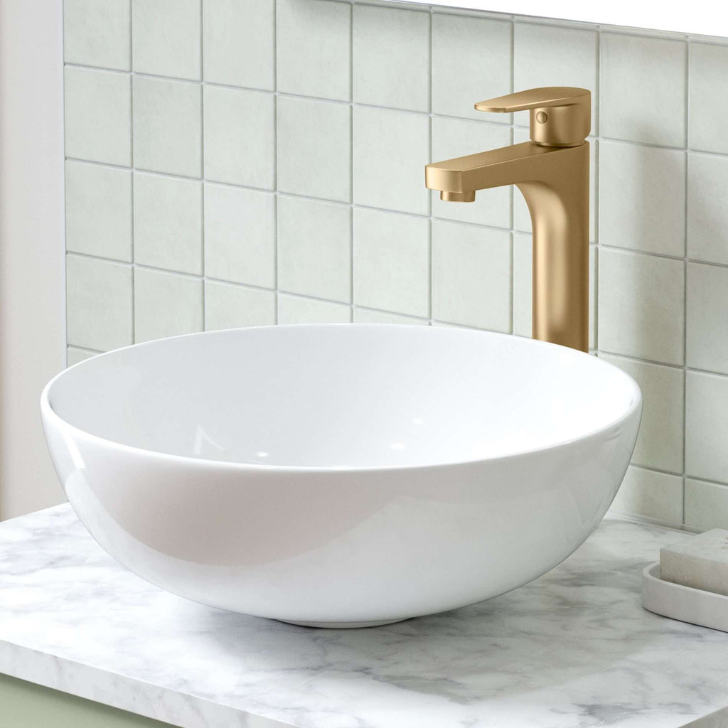 Sleek white bathroom sink with a modern gold faucet on a marble countertop against a tiled wall. Perfect for contemporary bathroom designs.