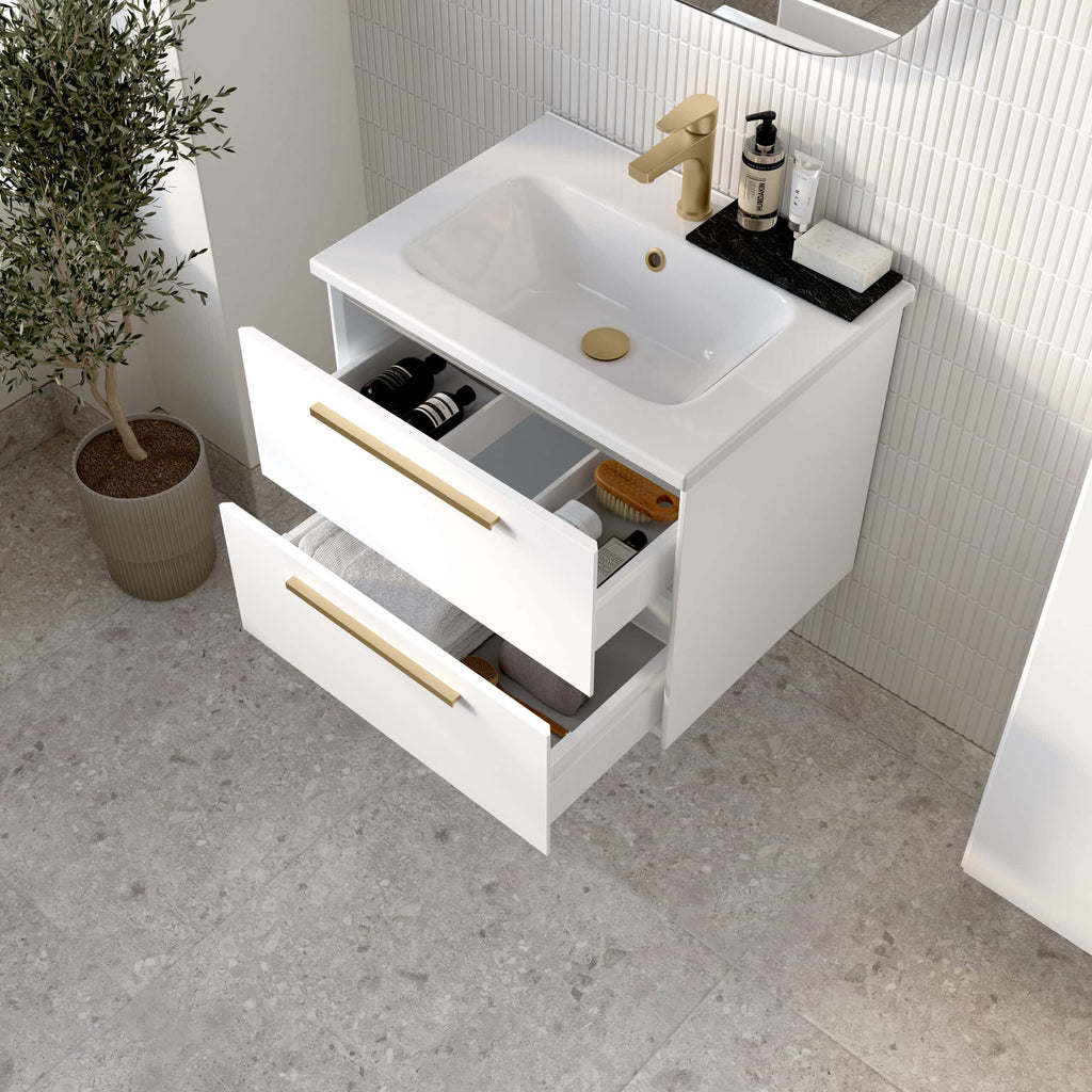 Sleek white bathroom vanity with integrated sink, gold hardware, and open drawers showing organised storage for toiletries and towels, set against a textured tile wall and stone floor.