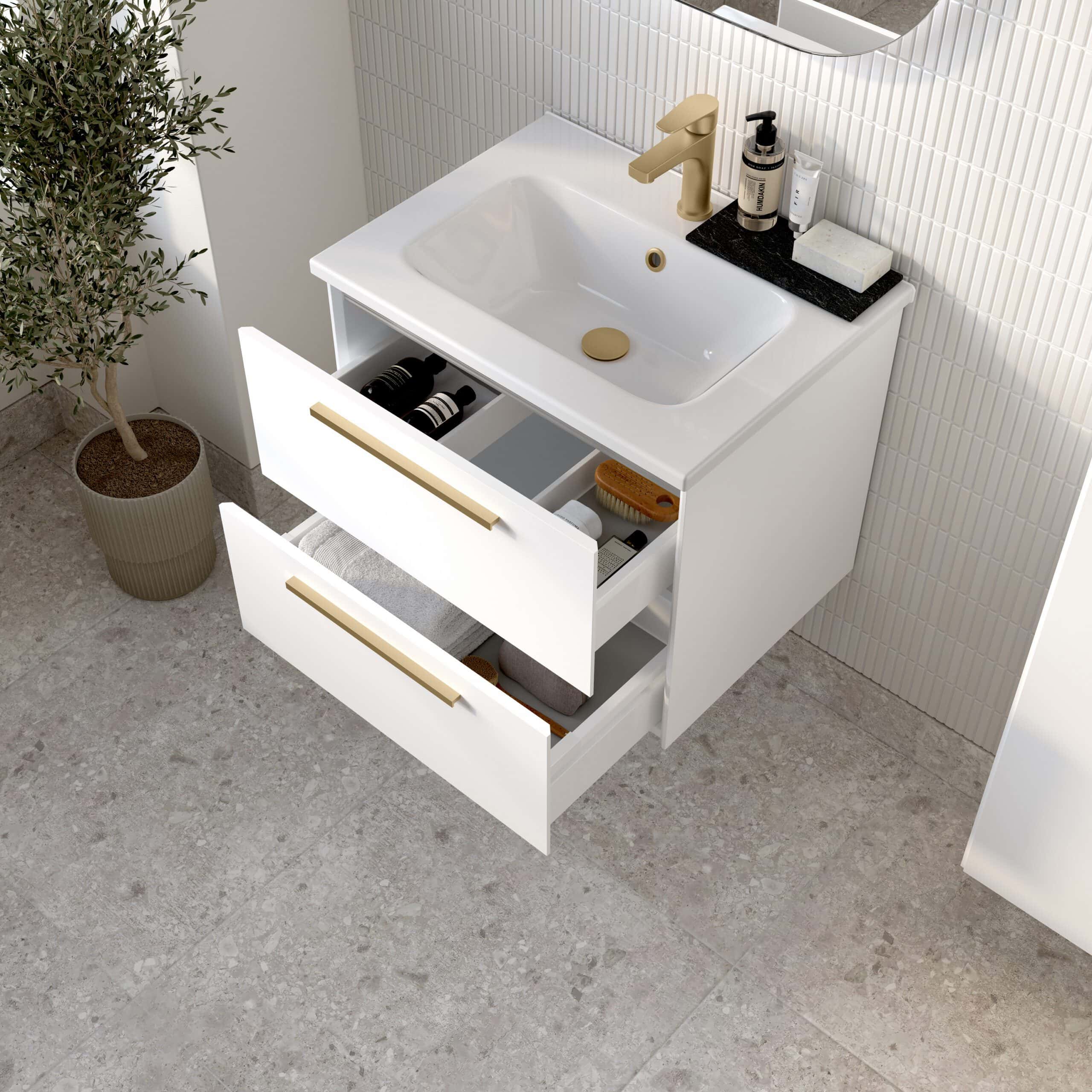 Sleek white bathroom vanity with integrated sink, gold hardware, and open drawers showing organised storage for toiletries and towels, set against a textured tile wall and stone floor.