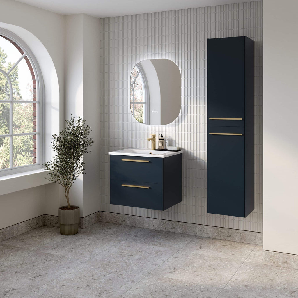 Elegant navy blue bathroom vanity with sleek gold handles, modern mirror with backlit LED, and a tall matching storage cabinet set against a textured white tiled wall in a bright, stylish bathroom.