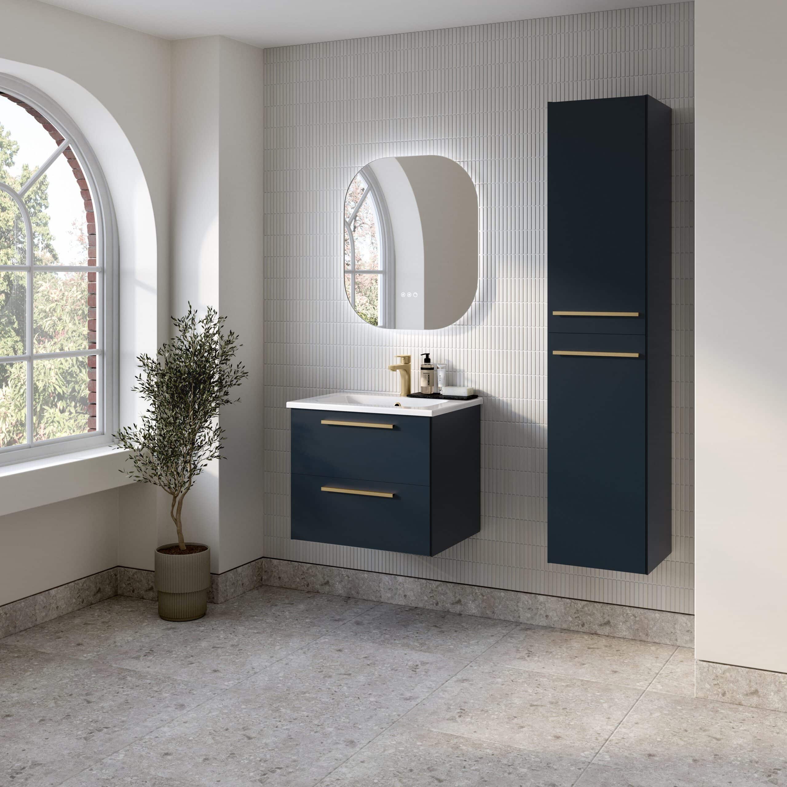 Elegant navy blue bathroom vanity with sleek gold handles, modern mirror with backlit LED, and a tall matching storage cabinet set against a textured white tiled wall in a bright, stylish bathroom.