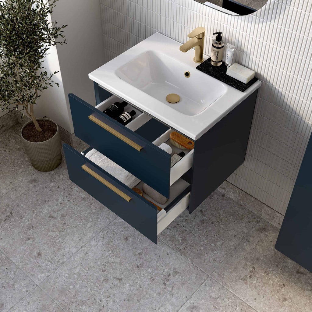 Modern bathroom vanity unit with a white sink, brass hardware, and open drawers filled with toiletries, set against a textured wall with a potted plant nearby.