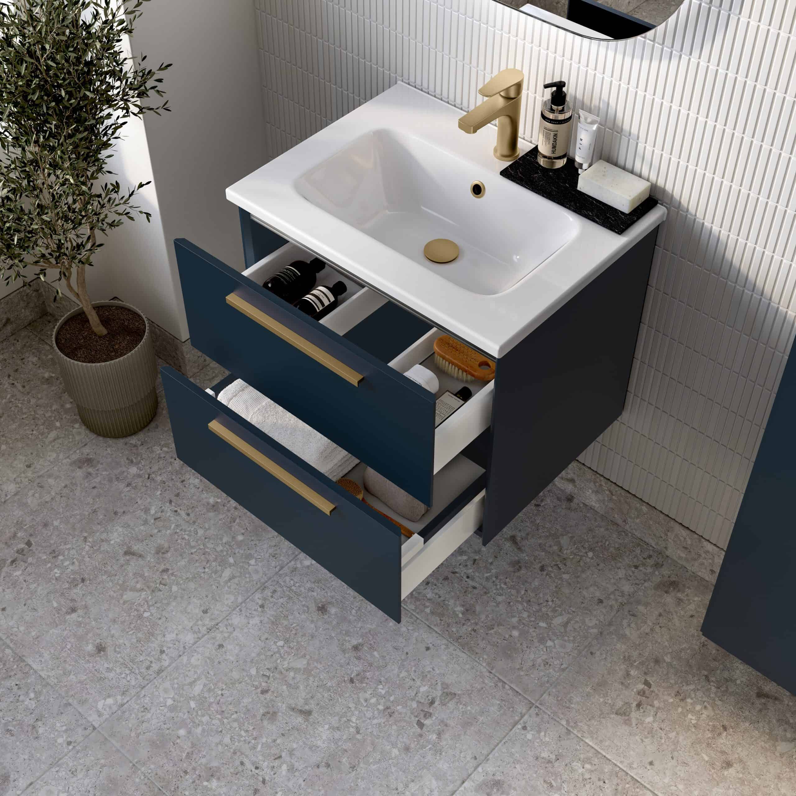Modern bathroom vanity unit with a white sink, brass hardware, and open drawers filled with toiletries, set against a textured wall with a potted plant nearby.