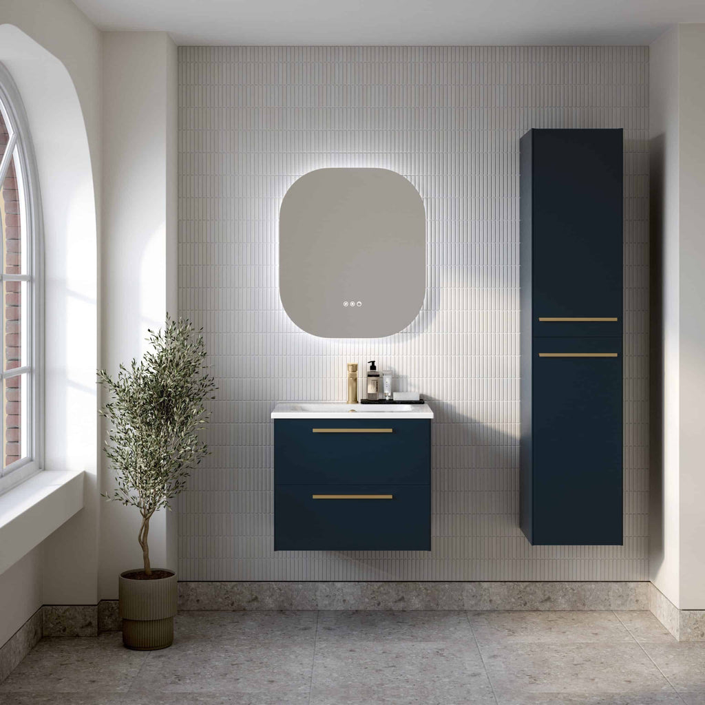 Modern navy blue bathroom vanity with gold handles and matching tall cabinet in a contemporary bathroom, featuring a white textured wall, a large mirror with backlighting, and a potted plant by the window for stylish decor.