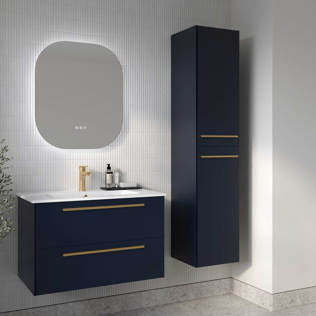Sleek navy blue bathroom vanity unit with gold handles and white countertop, paired with a tall matching cabinet, set against modern white tiled walls with backlit mirror for stylish bathroom design.