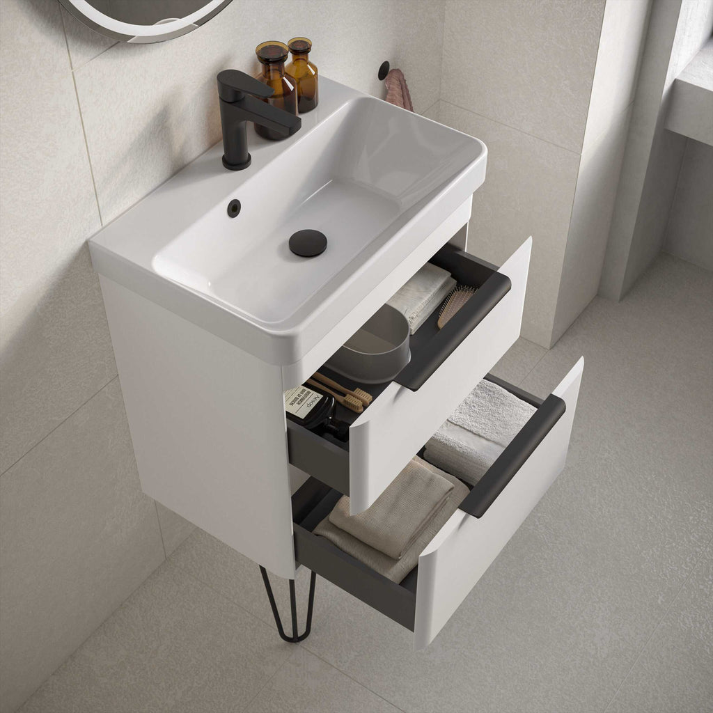 Modern white bathroom vanity with black handles, open drawers containing towels and toiletries, black sink tap, and a mirror, perfect for stylish bathroom storage solutions.