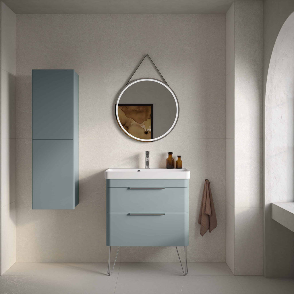 Sleek blue bathroom vanity unit with modern metallic handles and a wall-mounted cabinet in matching colour, stylish round mirror with LED lighting, beige tiled walls, and bathroom accessories.