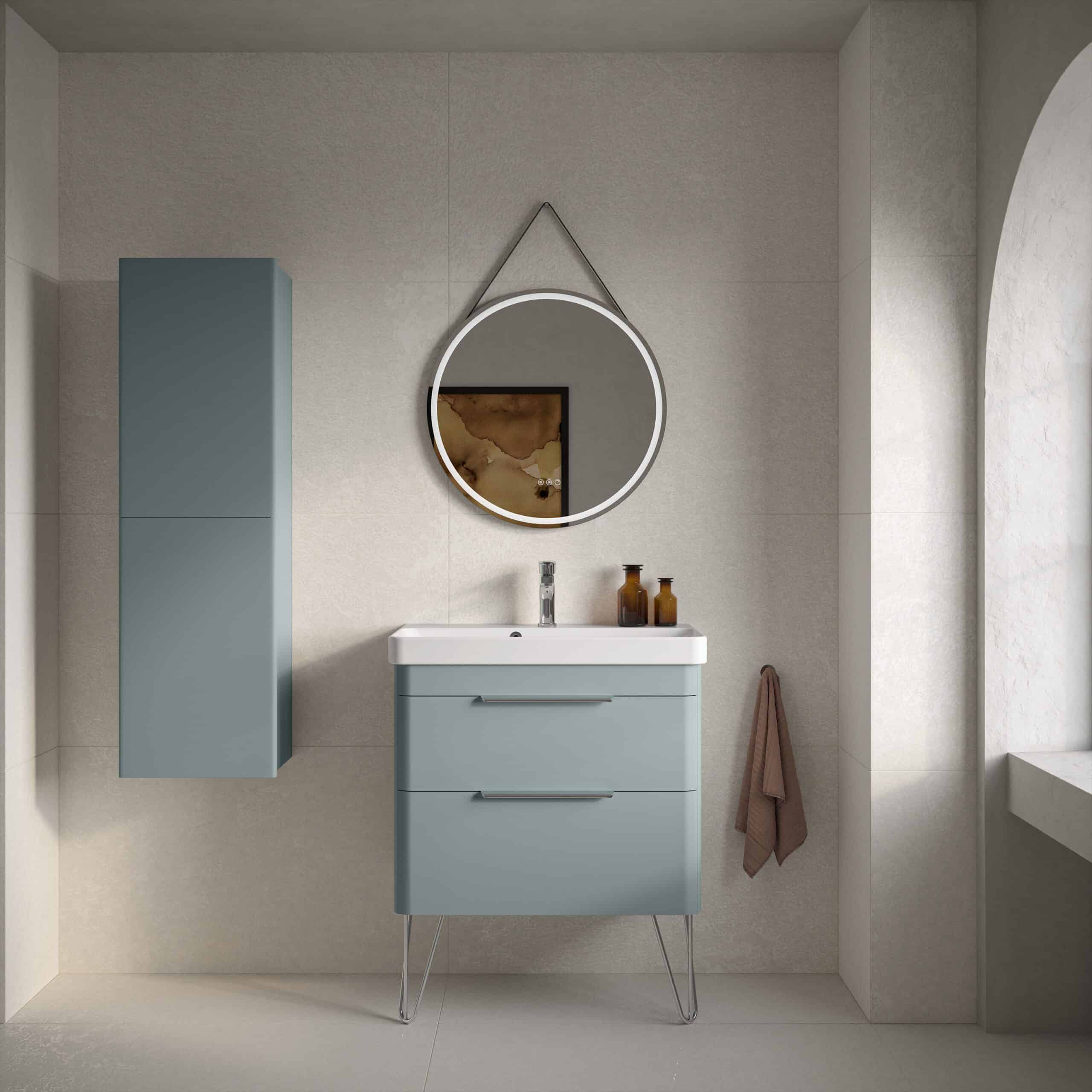 Sleek blue bathroom vanity unit with modern metallic handles and a wall-mounted cabinet in matching colour, stylish round mirror with LED lighting, beige tiled walls, and bathroom accessories.