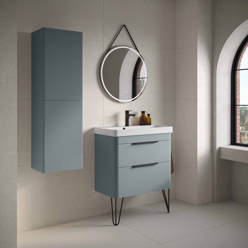 Sleek blue bathroom vanity unit with modern black handles, mounted cabinet, oval mirror with LED lighting, and stylish accessories in a contemporary bathroom setting.