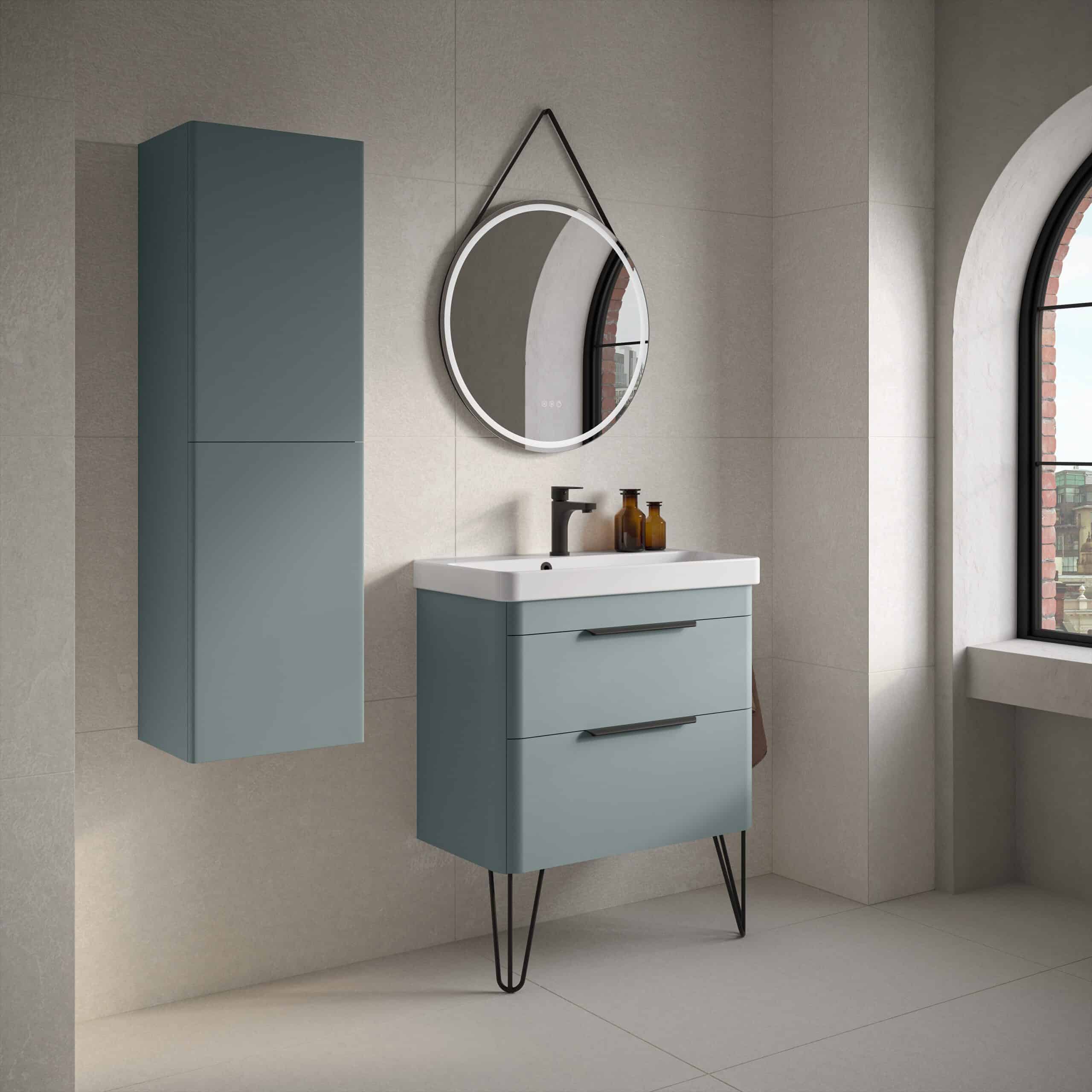 Sleek blue bathroom vanity unit with modern black handles, mounted cabinet, oval mirror with LED lighting, and stylish accessories in a contemporary bathroom setting.
