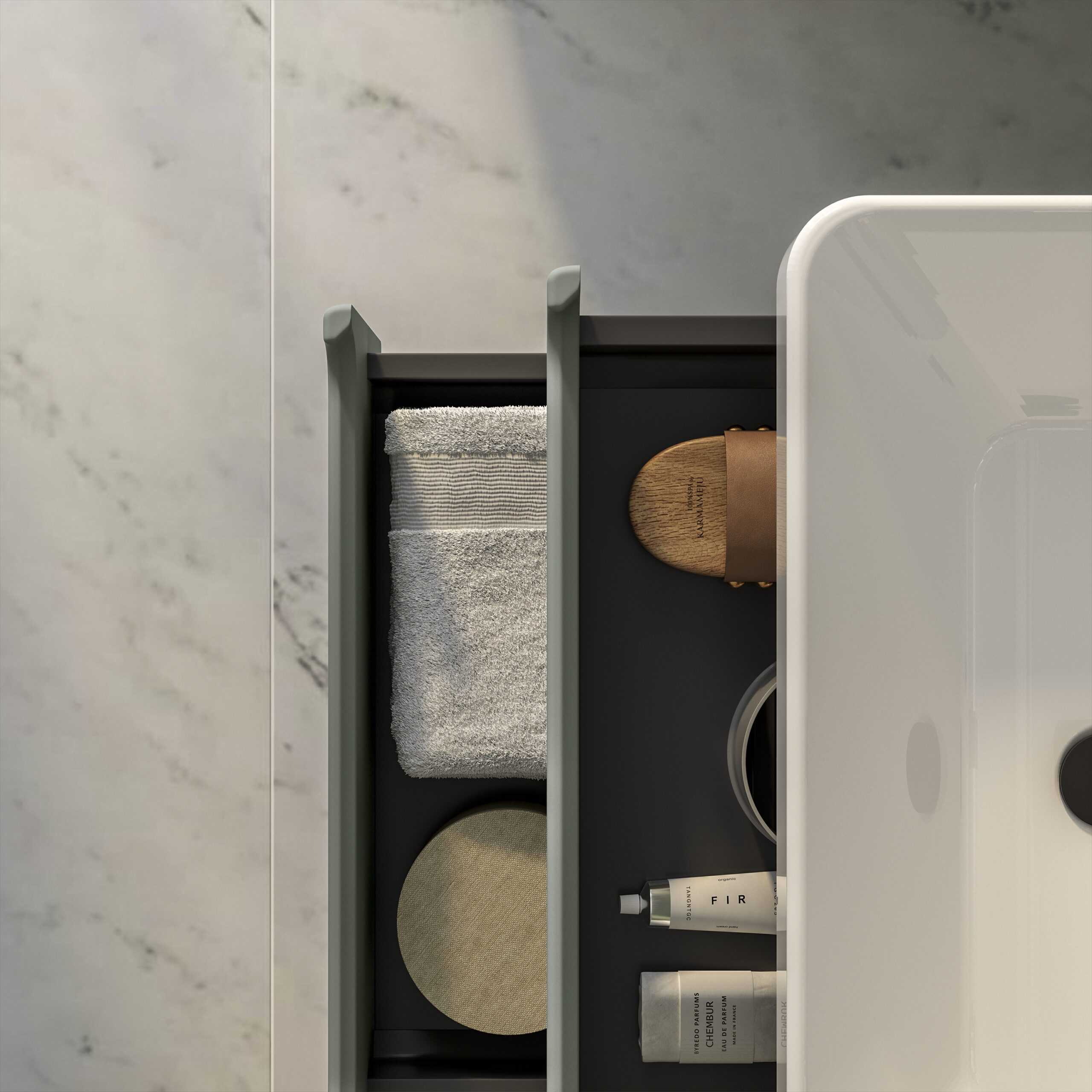 Minimalist bathroom storage drawer with grey dividers holding towel, wooden hairbrush, candles, and toiletries in a modern bathroom setting.