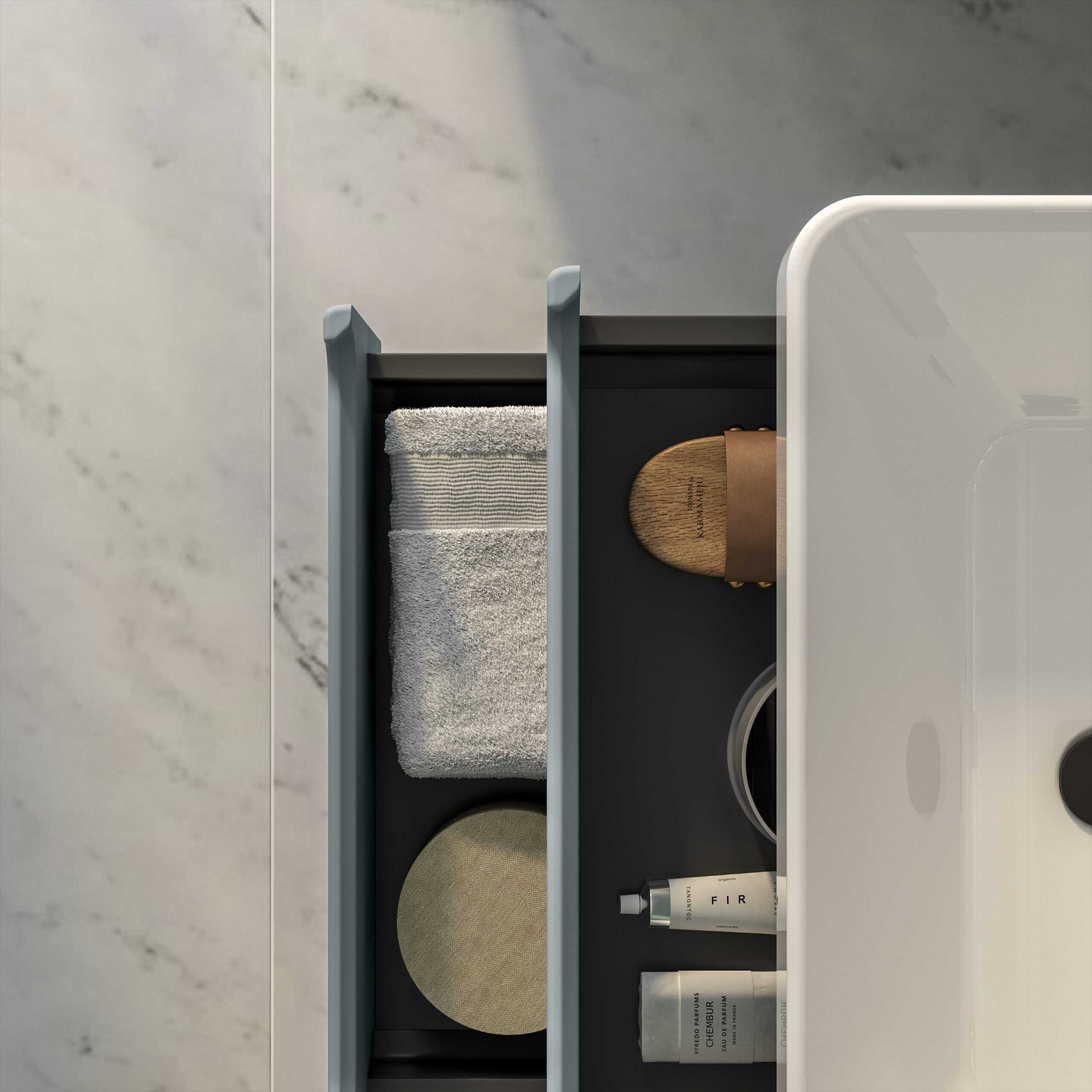 Minimalist bathroom countertop organisation with a dark storage tray holding a rolled towel, wooden brush, candles, and skincare products, featuring modern, clean design elements for a sleek bathroom look.